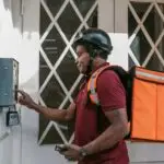 Delivery person with insulated bag pressing doorbell at entrance, providing home delivery service.