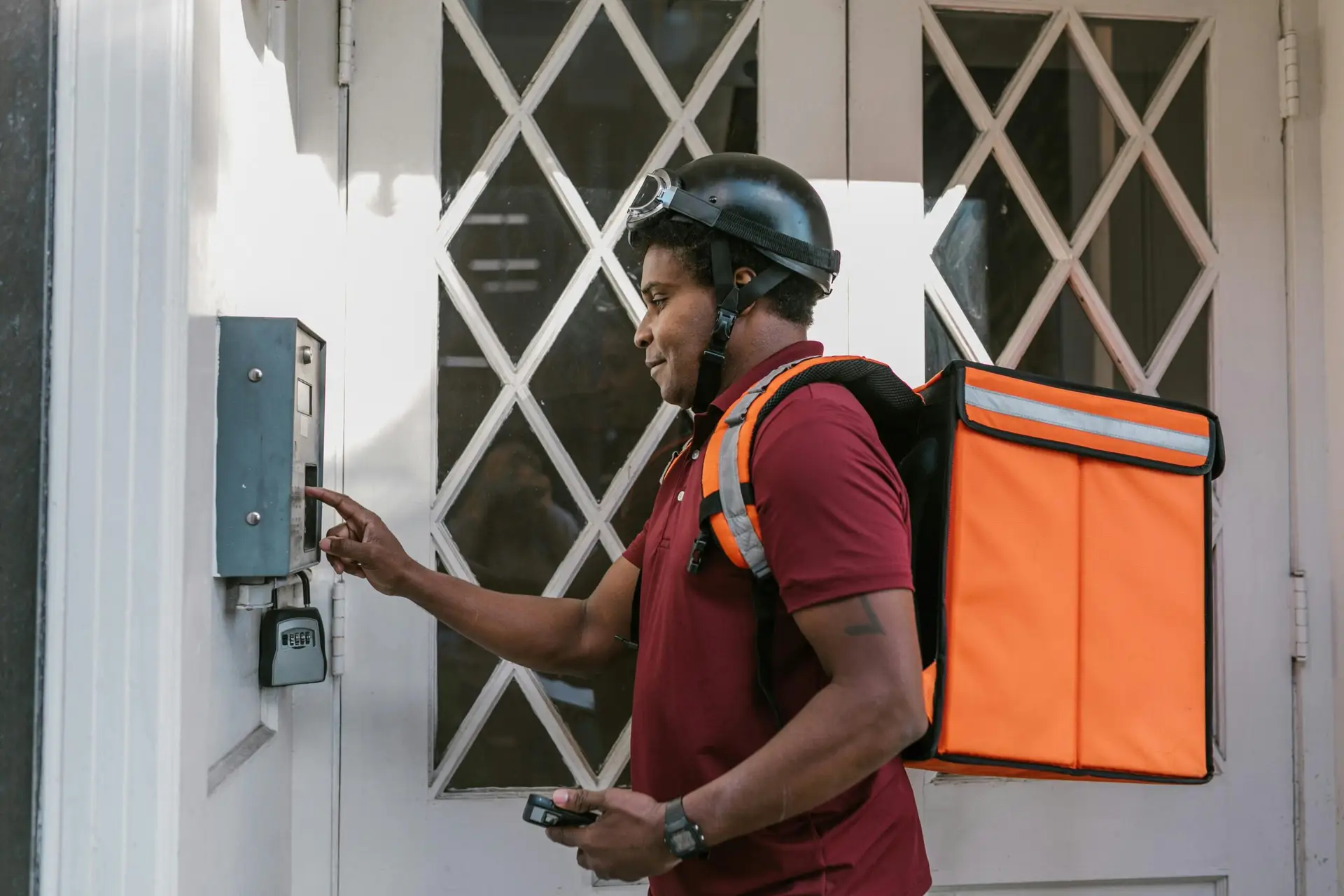 Delivery person with insulated bag pressing doorbell at entrance, providing home delivery service.